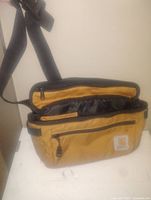 Carhartt fanny pack bag in tan with black zippers and adjustable strap shown open to reveal compartments.