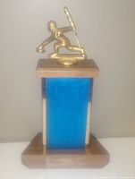 Photo showing the front of a vintage curling trophy with a gold-tone curler figure and blue rectangular panel on base.