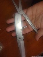 Open multi tool showing scissors and a blade in use, held in hand to show scale.