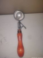 Photo showing the full ice cream scoop with polished metal scoop head and wooden handle on a white surface.