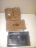 Photo showing three leather wallets: two light brown and one black, all from Roots brand, displayed on a flat surface.