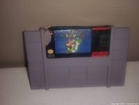 Photo of a gray Super Nintendo game cartridge for Super Mario World with a damaged label corner.