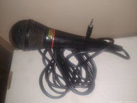 Photo of a black handheld microphone with a wired 1/4 inch jack plug cable, showing mesh grille and red ring on head.