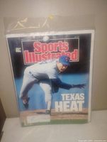 Photo of a vintage Sports Illustrated magazine with Nolan Ryan pitching on the cover and the headline 'Texas Heat'. The magazine is sealed in a clear protective bag.