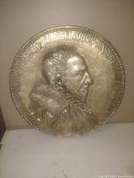 Single round chalkware wall plaque with relief profile of a Renaissance-style man and embossed text.