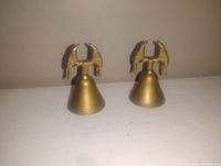 Pair of vintage brass bells each topped with a bird figurine, placed side by side on a white surface against neutral background