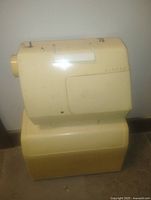 Side view of a cream-colored older Singer sewing machine on top of a yellow-beige hard plastic case.