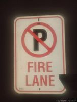 Metal No Parking Fire Lane sign with red and black lettering on white background, slight paint damage on lower right corner