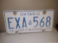 Photo of the 1973 Ontario license plate showing EXA 568 and 'KEEP IT BEAUTIFUL' slogan with some rust marks around mounting holes.