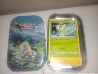 Metal collectible tin with Snivy artwork and open tin exposing a stack of Pokemon cards, top card is a Celebi card.