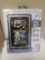 Front image of the sealed wireless color display weather forecast station box showing the digital display with time, date, weather forecast icons, temperature, and humidity readings along with feature highlights.
