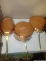 Three vintage Portugal made copper frying pans placed upside down showing their copper bases and brass handles on a white surface.