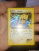 Hand-held photo of Rocket's Zapdos holo foil Pokemon card showing holographic shine and detailed attacks.