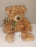 Photo of a small vintage teddy bear plush with light brown curly fur and a checkered scarf, seated upright.