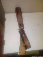 Photo showing a brown vintage pressed leather belt with a metal buckle laid flat on a white surface. The leather has a textured design and shows slight signs of use.