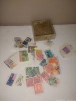A group of assorted vintage used postage stamps in various colors and designs, along with a small clear plastic box for storage.