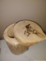 Close view of the wooden log box showing swing lid attached by a pin and First Nations style stamped figure on lid top.