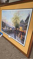 Framed print leaning against a wall showing Parisian street scene with Eiffel Tower in the background.
