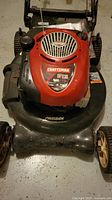 Front view of Craftsman lawn mower showing red Briggs & Stratton engine cover with Craftsman branding, black mower deck with 'Precision' label, and used condition.