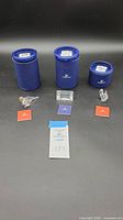 Three Swarovski crystal figurines displayed in front of three blue cylindrical containers and accompanied by certificates and original packaging materials.