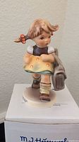 Front view of the Goebel Hummel 'School's Out' figurine on its original packaging showing the figure of a young girl walking with a satchel.