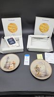 Two decorative plates with original boxes and certificates, front view showing plate designs.