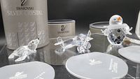 Three Swarovski crystal figurines displayed with original packaging: a clear crystal duck, airplane, and snowman with frosted details.