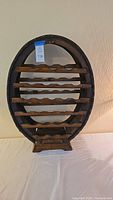 Front view of oval wooden wine rack with multiple rows to hold wine bottles, showing barrel metal trim and wood finish.