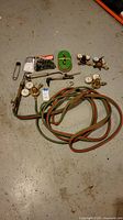 Photo of the entire oxy-acetylene torch kit including hoses, torch handle with gauges, regulators, nozzles, and accessories on a gray floor.