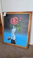 Framed canvas painting depicting a white naked female torso with a large pink rose and green leaves for a head, against a gradient black to blue background, signed by L. Chang in the bottom right corner.