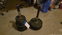 Two adjustable dumbbells with multiple weight plates stacked on and around the handles on garage floor.