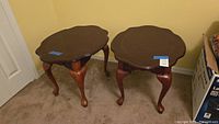 Two wooden end tables side by side showing the scalloped tops and cabriole legs.