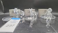 Three Swarovski crystal animal figurines (fox, hound, poodle) displayed with original packaging in background.