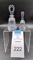 Two Swarovski crystal bells, one large and one small, placed on a clear acrylic stand with auction tag.