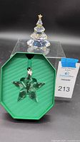 Swarovski clear crystal Christmas tree figurine with gold decorative accents and star topper behind star ornament display.