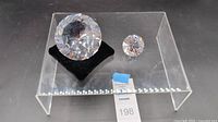 Two Swarovski crystal diamond-shaped figurines, large and small, displayed on a clear acrylic stand with lot tag visible.