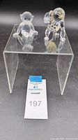 View showing two Swarovski crystal monkey figurines sitting and standing on a clear acrylic display stand.