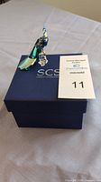 Peacock figurine displayed on blue SCS Swarovski storage box with auction card