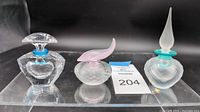 Set of three Swarovski crystal perfume bottles displayed on a clear stand with auction lot tag present