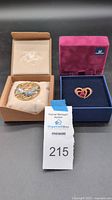 Both Swarovski crystal pins displayed with their original boxes and a lot number tag labeled 215