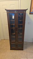 Front view of tall wooden stereo cabinet with glass doors showing shelves inside and two smaller glass doors at bottom.