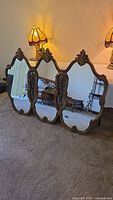 Full view of the triple panel mirror leaning on floor with decorative lamp and furniture in background, showing overall structure and condition.