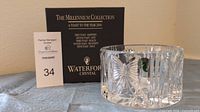 Clear, cut crystal champagne bottle coaster shown with original black box packaging with 'The Millennium Collection: A Toast to the Year 2000' text and Waterford Crystal logo. The coaster features intricate, deep cut crystal design and a sticker showing Made in Ireland.