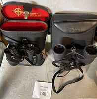 Both pairs of vintage binoculars side by side with their respective cases.
