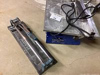 Anvil Manual Tile Cutter with metal base and blue handle grips on sliding rails, viewed from above.