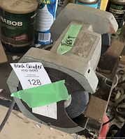Photo of the bench grinder showing the left grinding wheel with partial green tape and lot number tag.