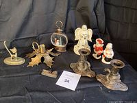 Full view of all items on black cloth backdrop including brass swan candle holders, brass leaf candle holder, brass cat ring holder, angel figurine, Mr & Mrs Claus salt and pepper shakers, snowman snow globe and miniature train.