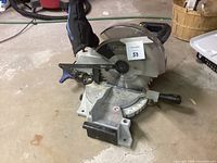 Metal Delta 10 inch miter saw with blade guard, blue adjustment knobs, angle base, and dust bag, photographed on a concrete floor.