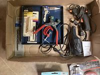 Box containing Dremel engraver, glue gun, grommet tool, hardware, and wood bit.