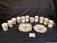 Front view of all 11 bone china mugs arranged in a row behind 2 serving plates on a black background